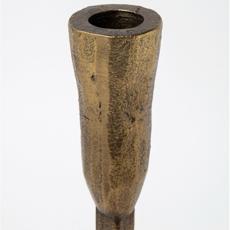 Close-up of the Levi Gold Iron Candlestick, a textured, cylindrical brass piece featuring a hollow, circular opening at the top. Exuding rustic elegance, its surface displays a rough, hammered appearance with a matte finish. The candlestick tapers slightly towards the bottom and is set against a plain white background.