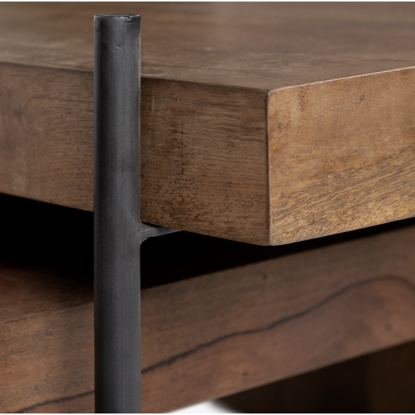 A close-up of a wooden table crafted from solid Mango wood features a thick tabletop with a natural wood grain texture. The edge showcases layered wood construction. A vertical, black metal support beam, boasting a smooth, matte finish, is attached to the side of the table. This piece bears a striking resemblance to the Thomas Nesting Coffee Tables in style.