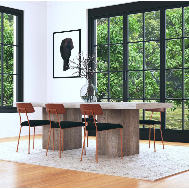 A modern dining room showcases the Arizona Concrete 94" Dining Table with a gray concrete laminate finish, surrounded by four wooden chairs with black cushions. A vase filled with branches decorates the table. Large, grid-patterned windows provide a view of a lush, green outdoor landscape. An abstract monochrome art piece adorns the wall.