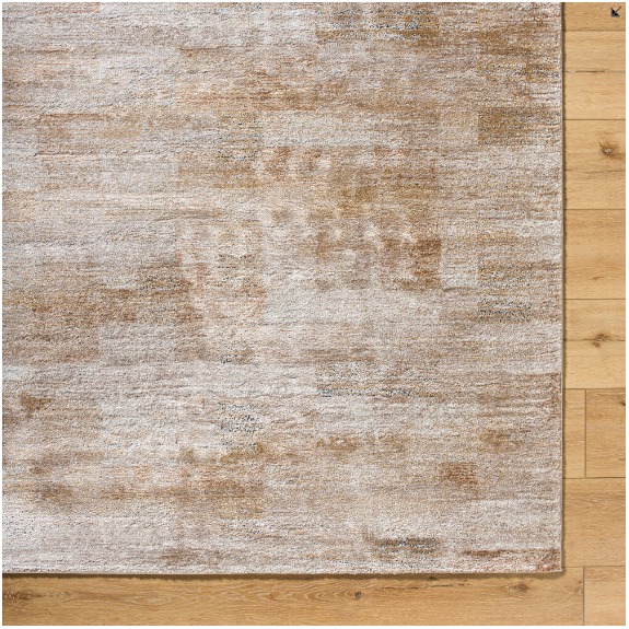 A close-up view of the Sahara Machine Woven Rug on a wooden floor highlights its light brown and beige hues and subtle abstract pattern. This high-pile design is crafted from a soft, textured material that blends seamlessly with the warm-toned wooden planks, offering exceptional durability.