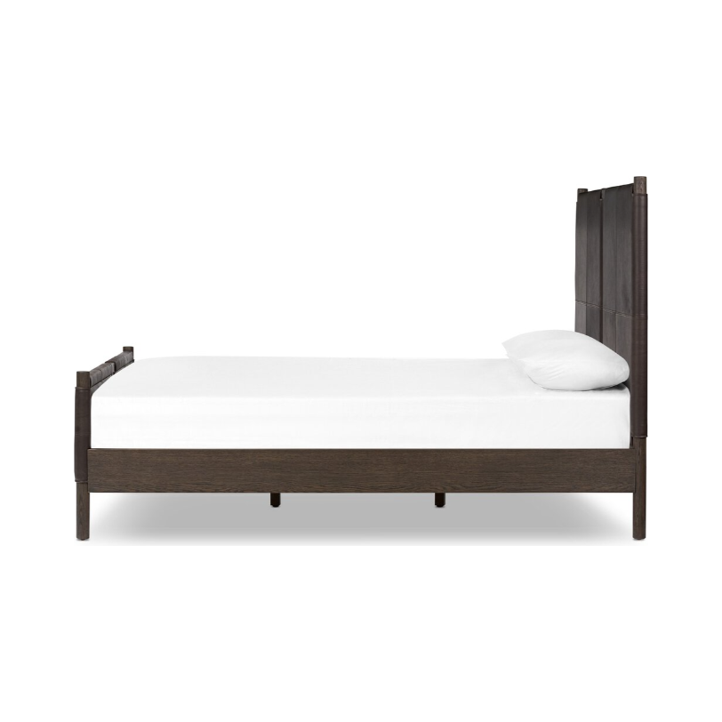 Side view of the Valencia Haven Bed highlights its safari-inspired elegance. This wooden bed frame in a dark finish boasts a high headboard and a low footboard adorned with vertical panel detailing. Styled with a plain white fitted sheet and a single white pillow, it radiates modern simplicity.