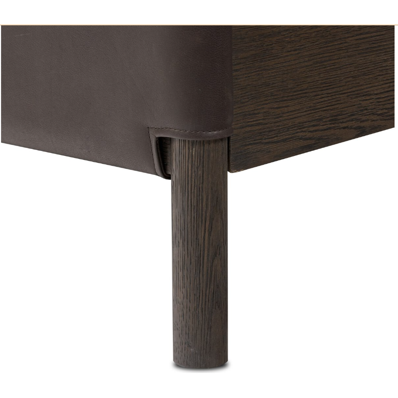 Close-up of a corner of the Valencia Haven Bed, featuring a cylindrical wooden leg and frame with visible grain. The finely crafted upcycled leather cover enhances its safari-inspired elegance.