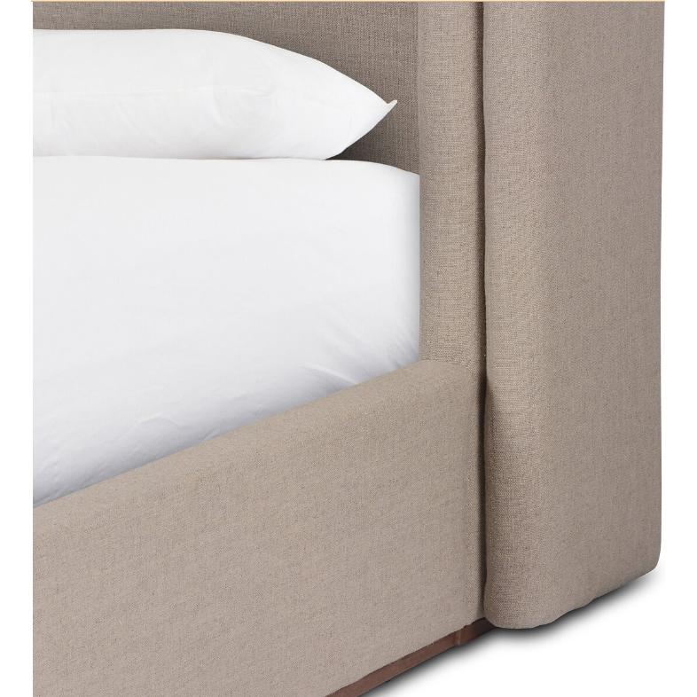 A close-up view of a corner of the Celeste Bed highlights its beige upholstery. This bed showcases a shelter-style headboard and a natural wood plinth base, with its textured fabric adding to the aesthetic. Two white pillows sit atop the partially visible mattress, enhancing its modern, minimalist elegance.