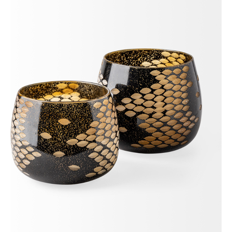 The Marina Black and Gold Glass Vase boasts an elegant design with its dark glass surface adorned in a glossy finish, featuring golden oval patterns that evoke the appearance of reptile scales. The interior shimmers with gold accents, creating an opulent charm when set against a light gray backdrop, reminiscent of finely crafted glassware.