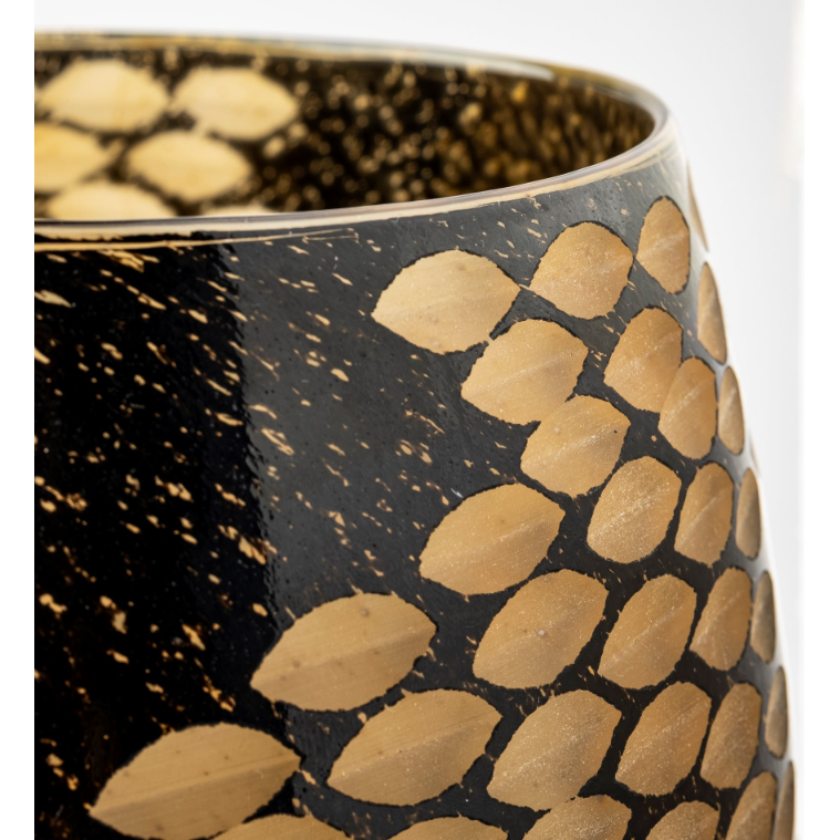 The Marina Black and Gold Glass Vase is shown in a close-up, set against a black background embellished with gold leaf patterns. Its intricate design showcases repeated, overlapping elliptical shapes, creating a textured appearance. The vase's glossy surface subtly reflects light, focusing the photo on its striking decorative details.