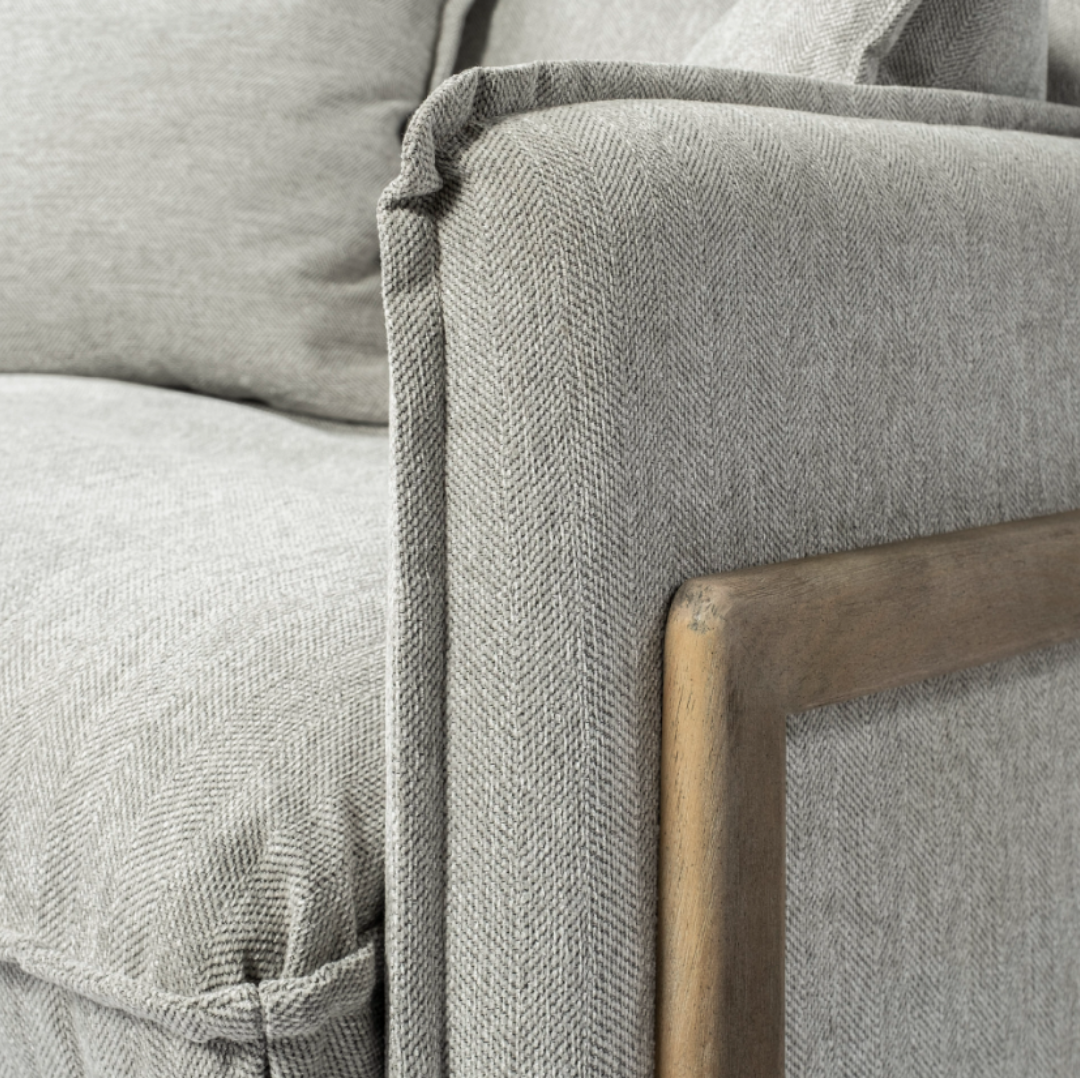 A close-up of the Veyra Plush Upholstered Armchair in Frost Grey showcases sophisticated comfort with its wooden frame. The subtle herringbone pattern exudes modern luxury, focusing on the corner to highlight its texture, plush cushion, and neatly stitched seams.