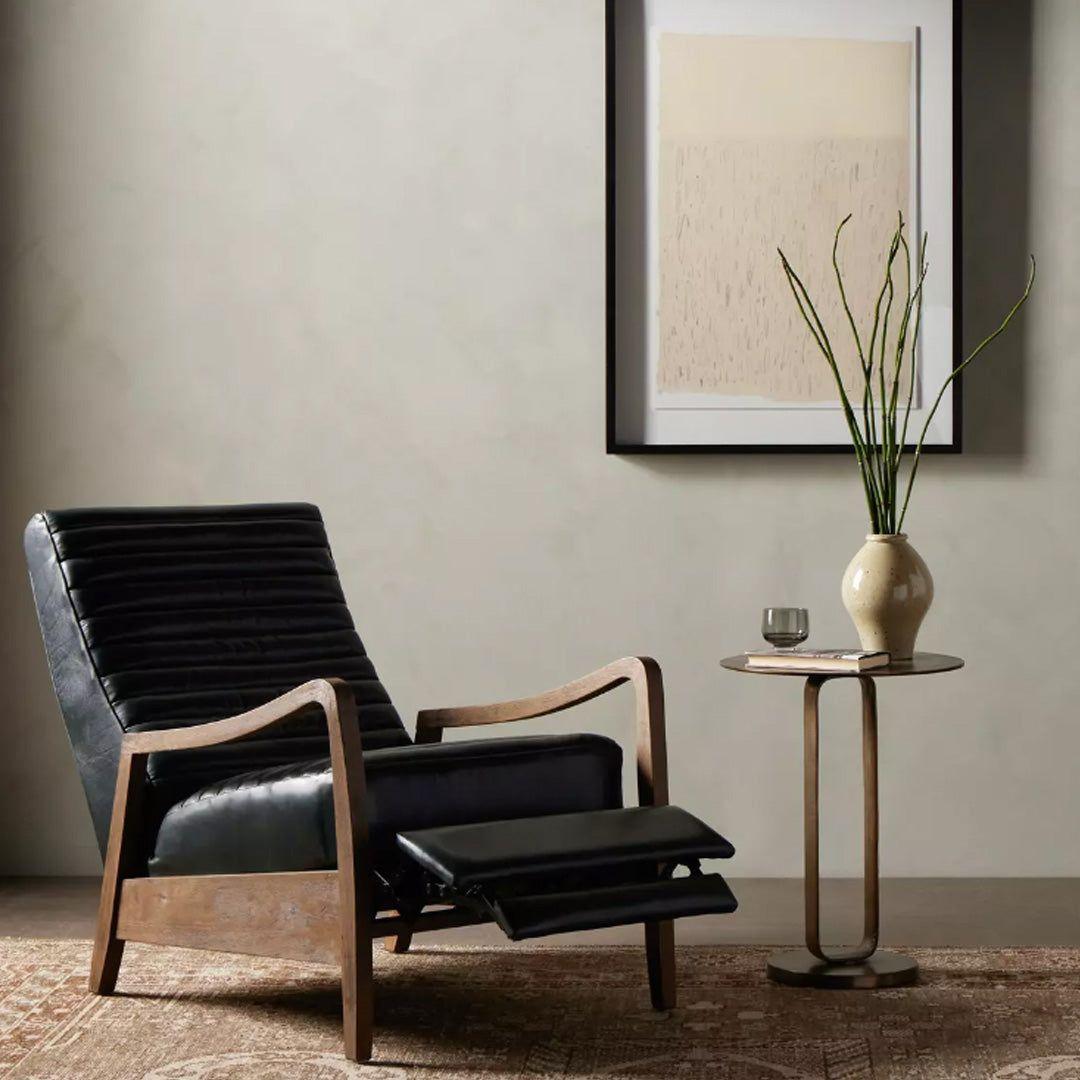 A modern living space with the Terra Leather Recliner in black, wooden arms and base, a round side table with a beige vase of green stems, small glass, neutral walls, textured rug, and abstract framed art for sleek mid-century style.