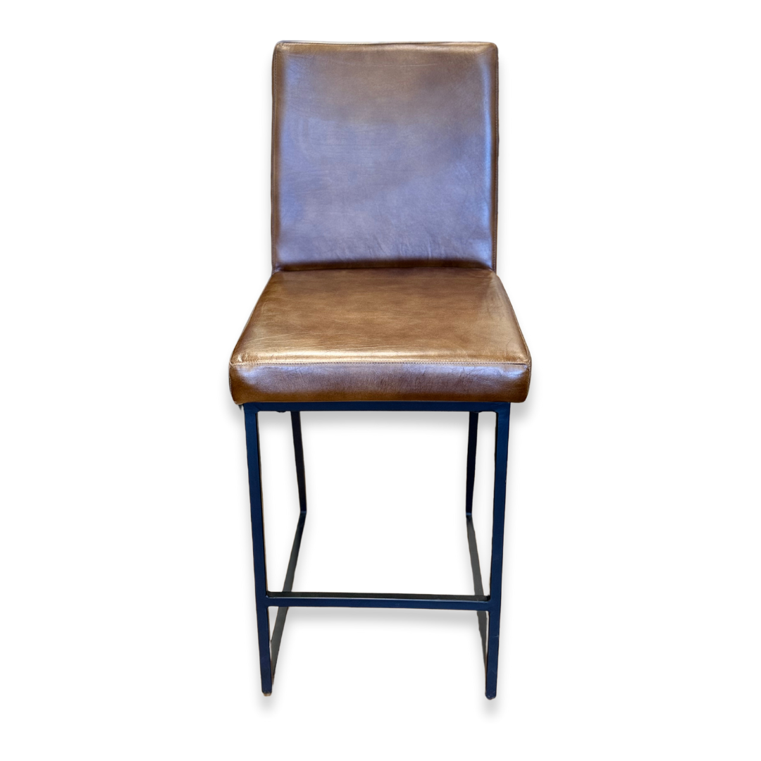 Theodore Leather Counter Stool showcases a brown leather seat with a cushioned backrest and an iron base with four black legs and horizontal supports, facing forward against a white background.