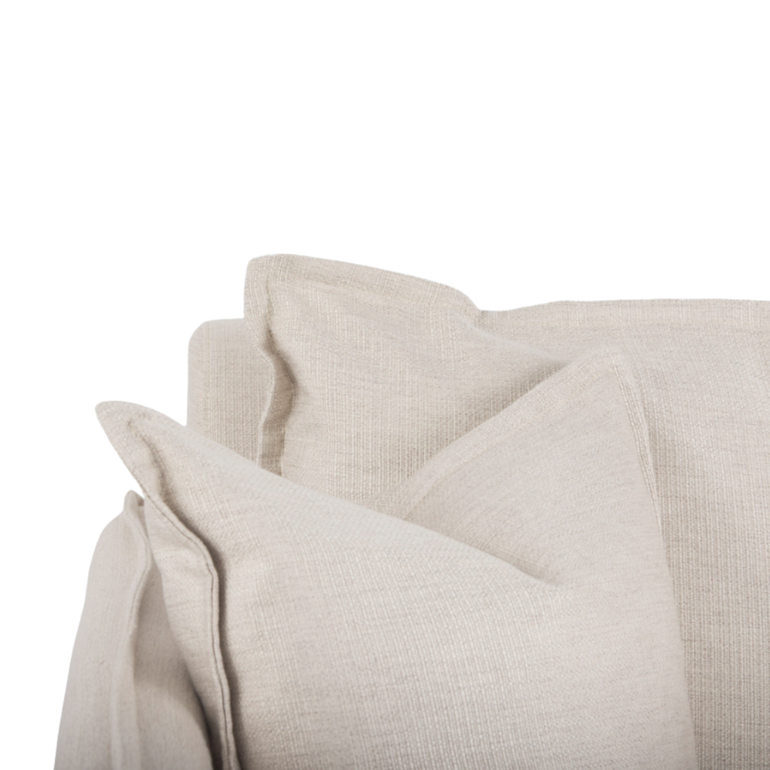 Close-up of a Veyra Plush Upholstered Armchair in beige, featuring three large square cushions that promise comfort. The soft, textured upholstery gives a cozy and inviting appearance, with slightly overlapping layers for added style. A solid oak finish enhances the plain backdrop setting.