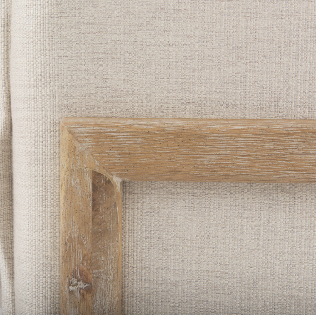 A close-up of textured fabric draped over the Veyra Plush Upholstered Armchair in beige reveals a natural off-white hue. The solid oak frame, with its light brown and visible grain, showcases a touch of rustic charm through slight wear and emphasizes the materials' textures.