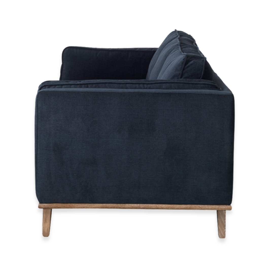 Side view of the Zinnia Mid-Century Modern Navy Fabric Sofa, showcasing two back cushions, reversible seats, straight armrests, and light wooden legs. Features plush comfort and clean lines, photographed on a plain white background.