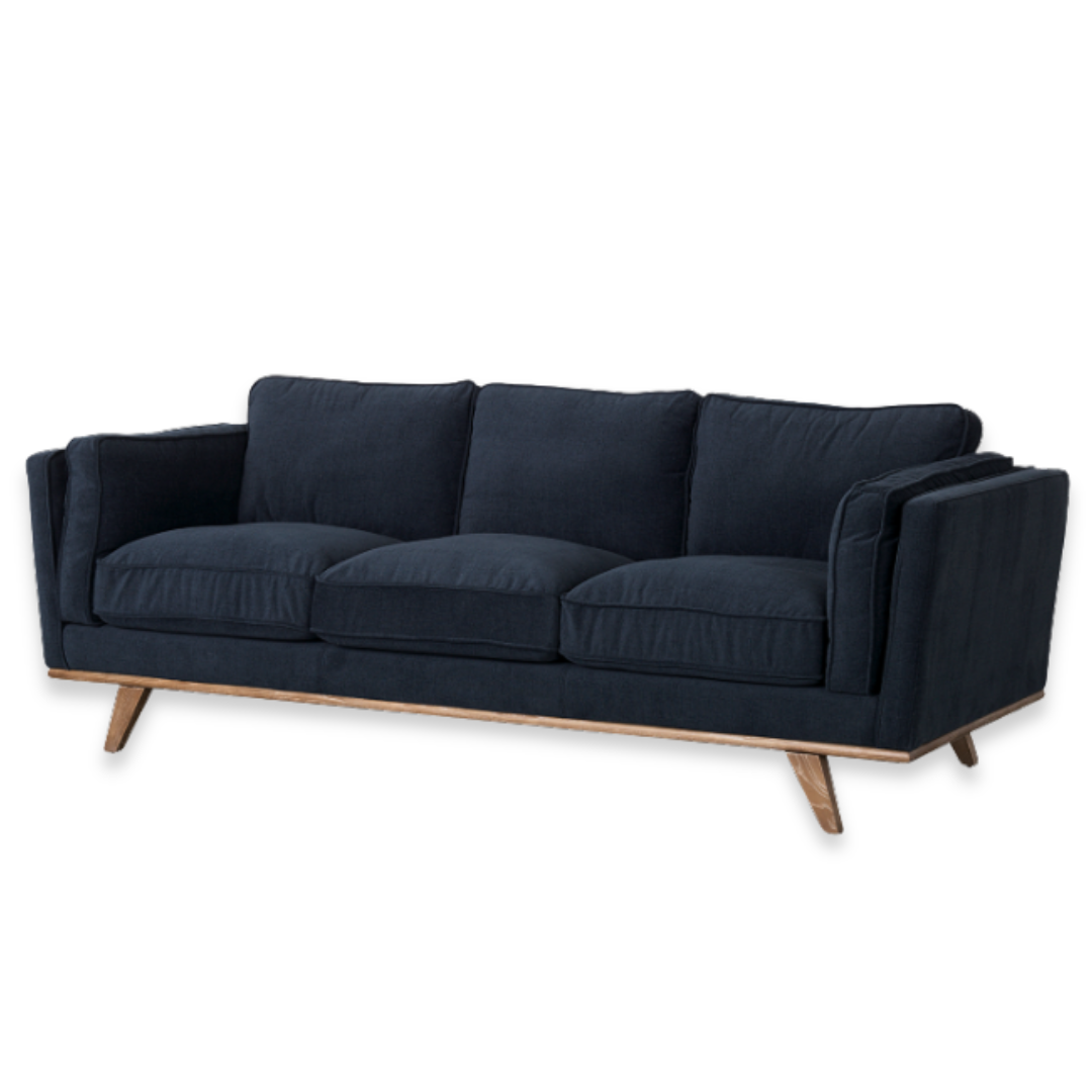 The Zinnia Mid-Century Modern Navy Fabric Sofa is a stylish three-seater with plush, reversible cushions, a low back, angled wooden legs, wide armrests, and navy upholstery. The sofa is shown on a plain white background.