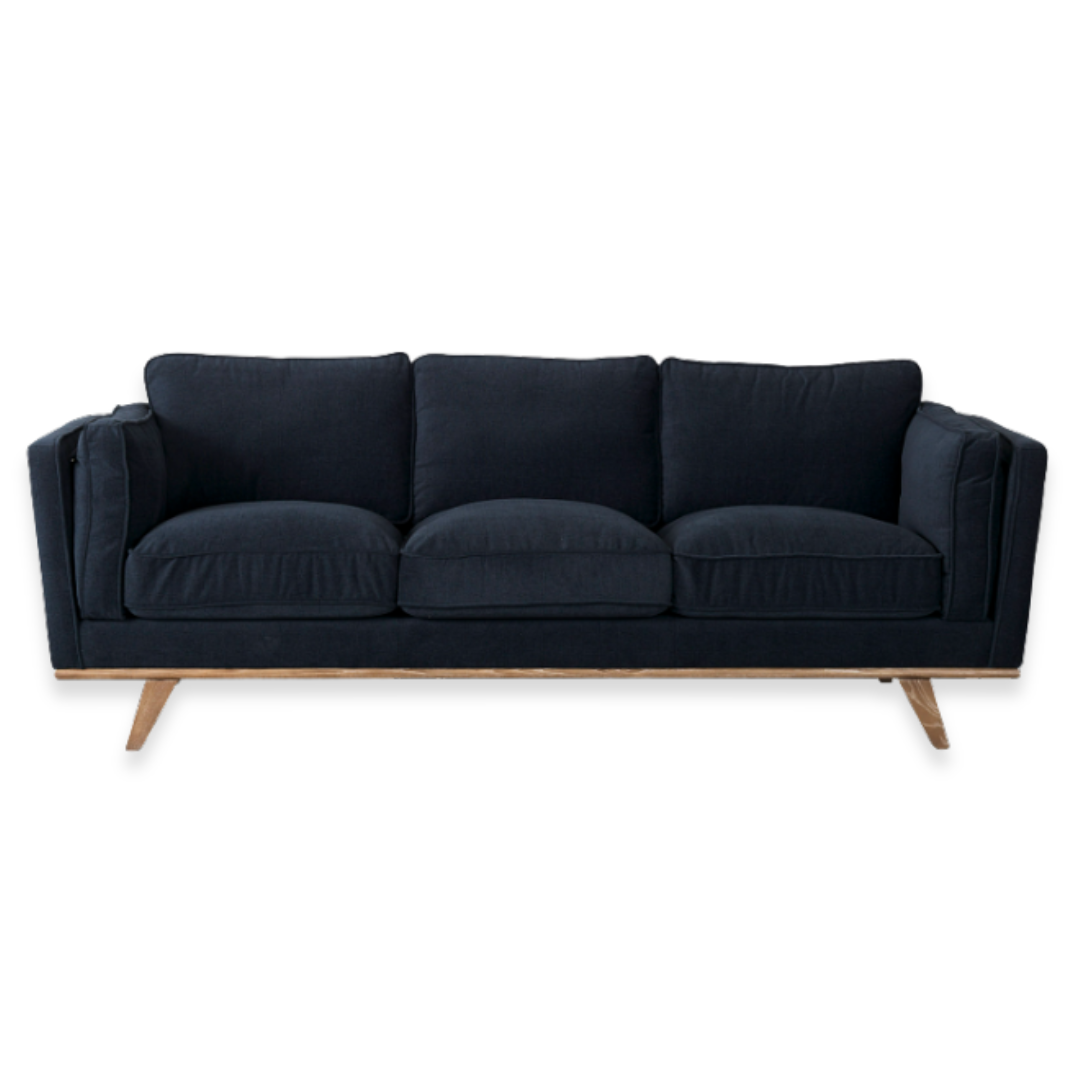 The Zinnia Mid-Century Modern Navy Fabric Sofa has plush, reversible cushions, low square armrests, and angled wooden legs. Its navy upholstery and clean lines offer a striking minimalist look on a plain white background.