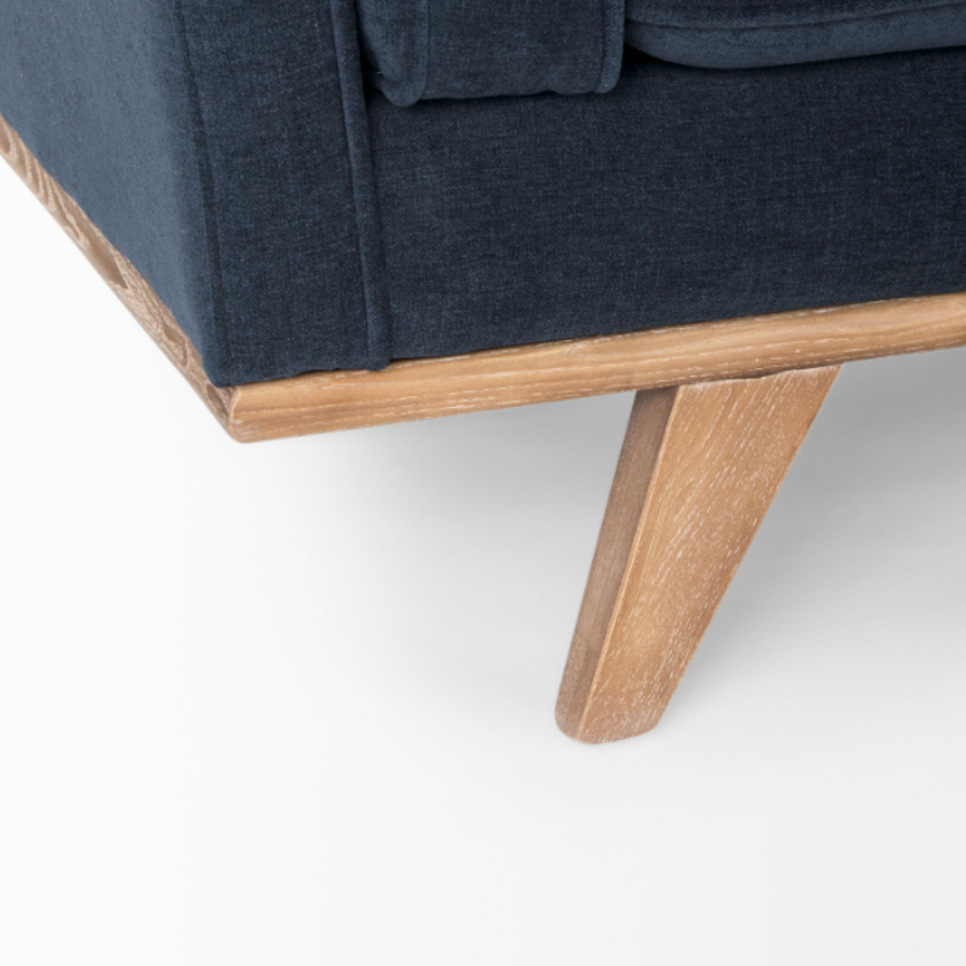 Close-up of the Zinnia Mid-Century Modern Navy Fabric Sofa, showing its navy upholstery and angled light wood leg. The image highlights the sofa's fabric texture and wood grain against a plain white background.