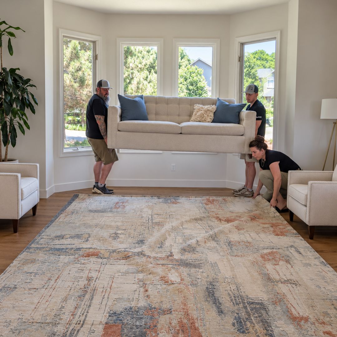 The Change Everything team positions a sofa and area rug during professional furniture placement in a client’s living room.