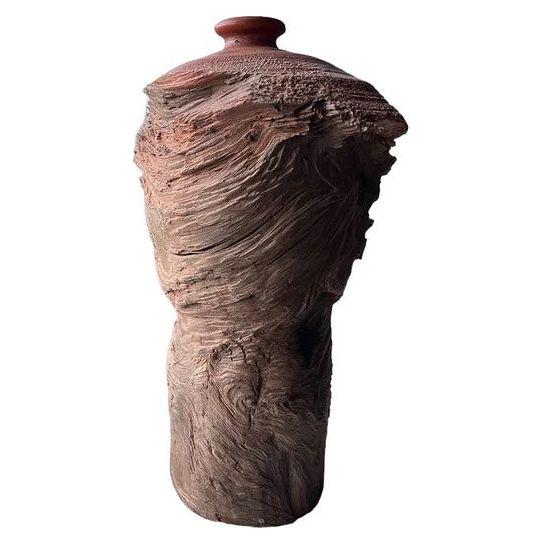 A tall, cylindrical, handcrafted ceramic Cloud Vase with a wavy, textured exterior resembling rough, undulating, and hand-carved wood. The top part is smoother with a reddish-brown color and a small, rounded mouth. This Cloud Vase's intricate surface creates an artistic, natural, and rustic appearance.
