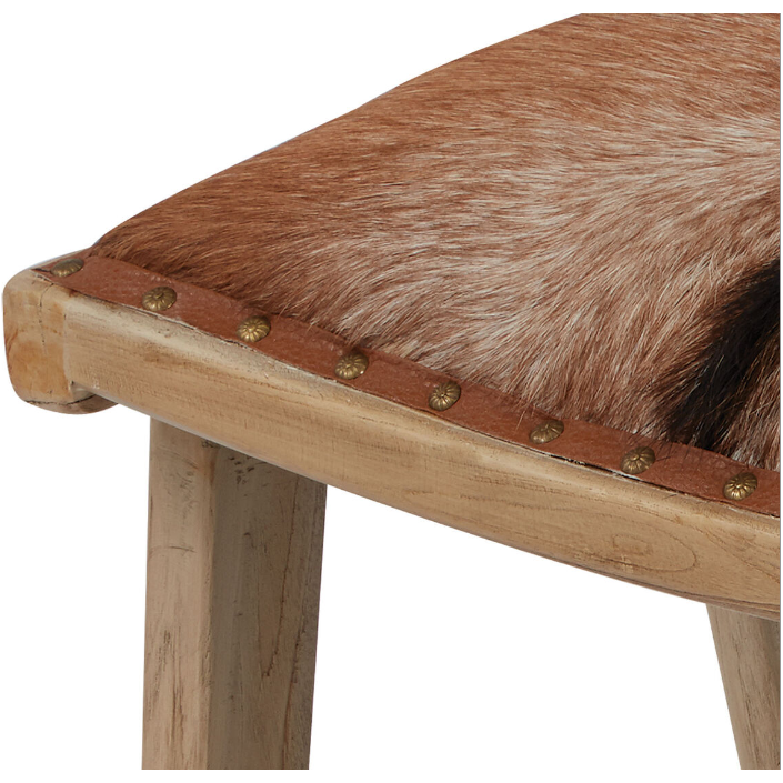 A detailed view of the Hair on Hide Accent Chair with Ottoman highlights a seat adorned in brown and white hair on hide leather, elegantly edged with brass studs. Featuring unfinished legs, it captures an organic modern aesthetic, serving as a stunning statement piece in any rustic environment.