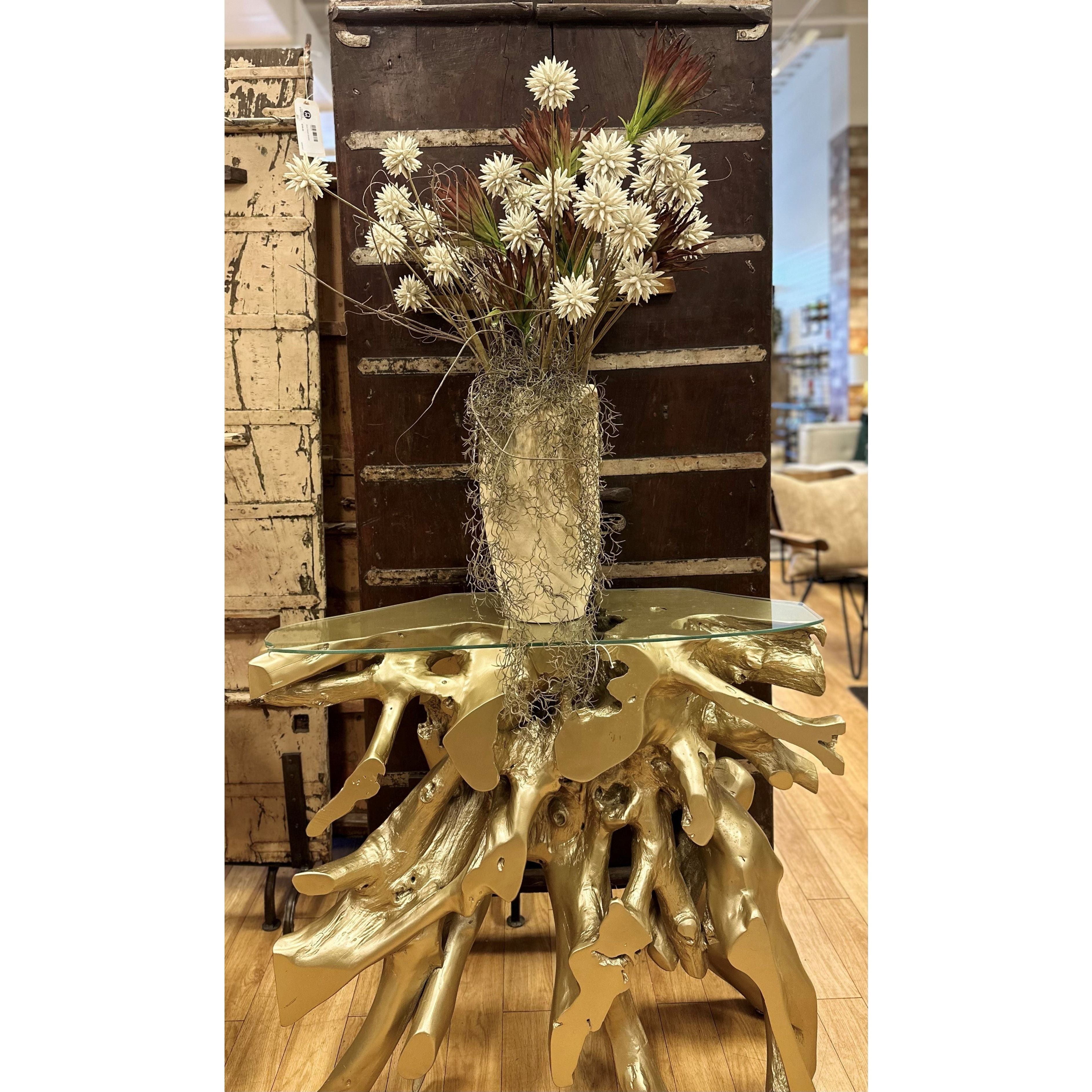 A Hillwood Console Table holds a vase of white flowers and red sprigs resembling a golden tree, with moss inside. Set against a dark distressed cabinet, the elegant display is complemented by the wooden floor and neutral-toned furniture in the background.