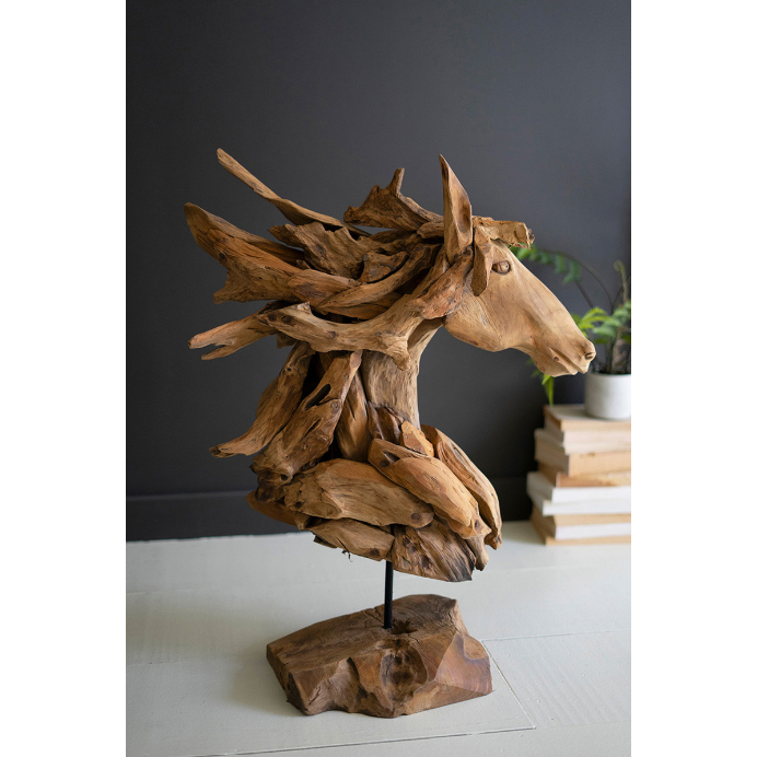 The Horse Head Sculpture is crafted from intertwined natural driftwood pieces, mounted on a flat base to achieve a rustic aesthetic. Set against a dark background, this piece exudes charm and elegance. The scene is complemented by stacked books and a plant partially visible to the right, making it an ideal decor choice for horse enthusiasts.