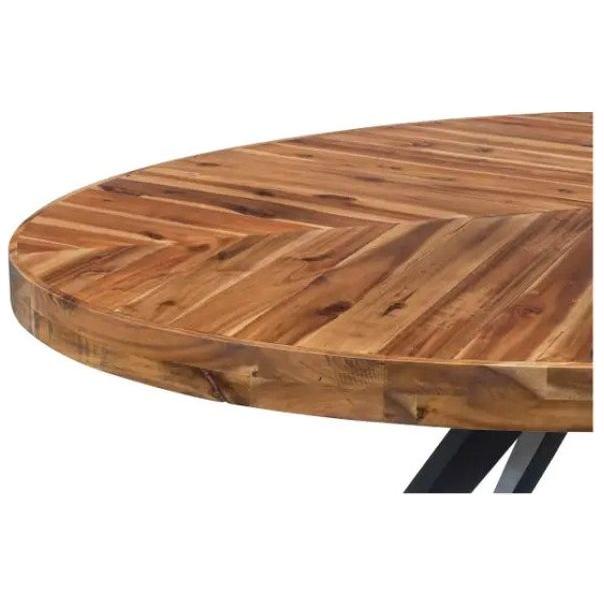 Close-up of the Park Oval Dining Table featuring a solid acacia top with a rich, natural wood grain finish. The parquet-patterned top showcases a smooth surface with interlocking wood pieces in varying shades, creating a chevron pattern. The edge of the table is slightly rounded, and part of the metal base legs is visible below.