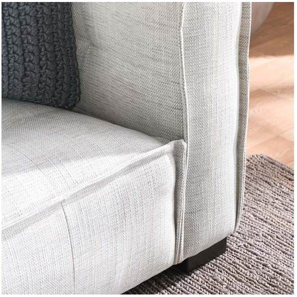 A close-up of the Princeton Sofa, Beige showing subtle button tufting and a textured gray cushion. It features visible seams on the armrests and dark wooden legs. The sofa is positioned on a gray woven rug over a wooden floor with sunlight casting soft shadows.