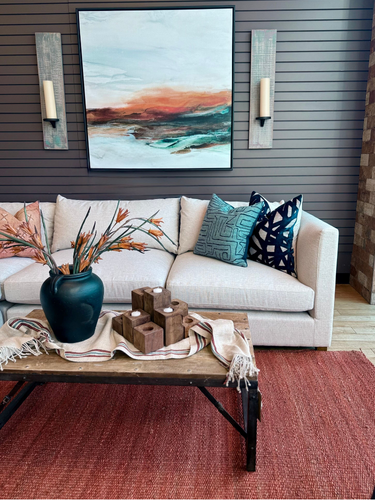 right side of sectional with blue throw pillow in front of an orange, blue and black abstract painting flanked with wood sconces.png