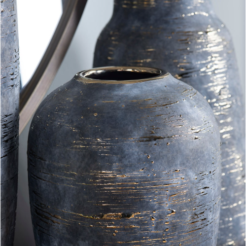 Close-up of the Triad Vase set, featuring dark blue ceramic vases with textured surfaces and shiny gold accents in the grooves. Focus is on the central vase, while its companions and a round mirror appear blurred in the background.