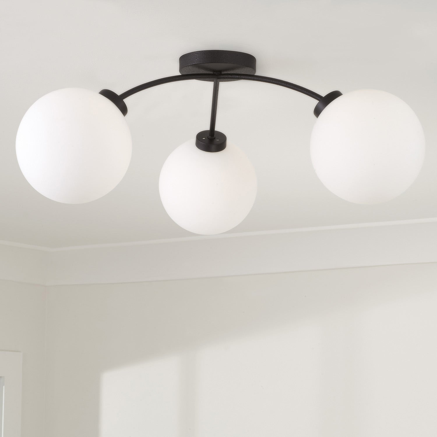 Ceiling light fixture with three white globe lights on a plain ceiling.