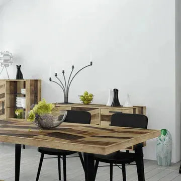 A modern dining room features a wooden table with a herringbone pattern and a sleek metal base, surrounded by four luxurious **Black Dining Chairs**. The table is adorned with a bowl of green apples and another of grapes. In the background, wooden shelves display decorative items, while a candelabra sits on a sideboard.