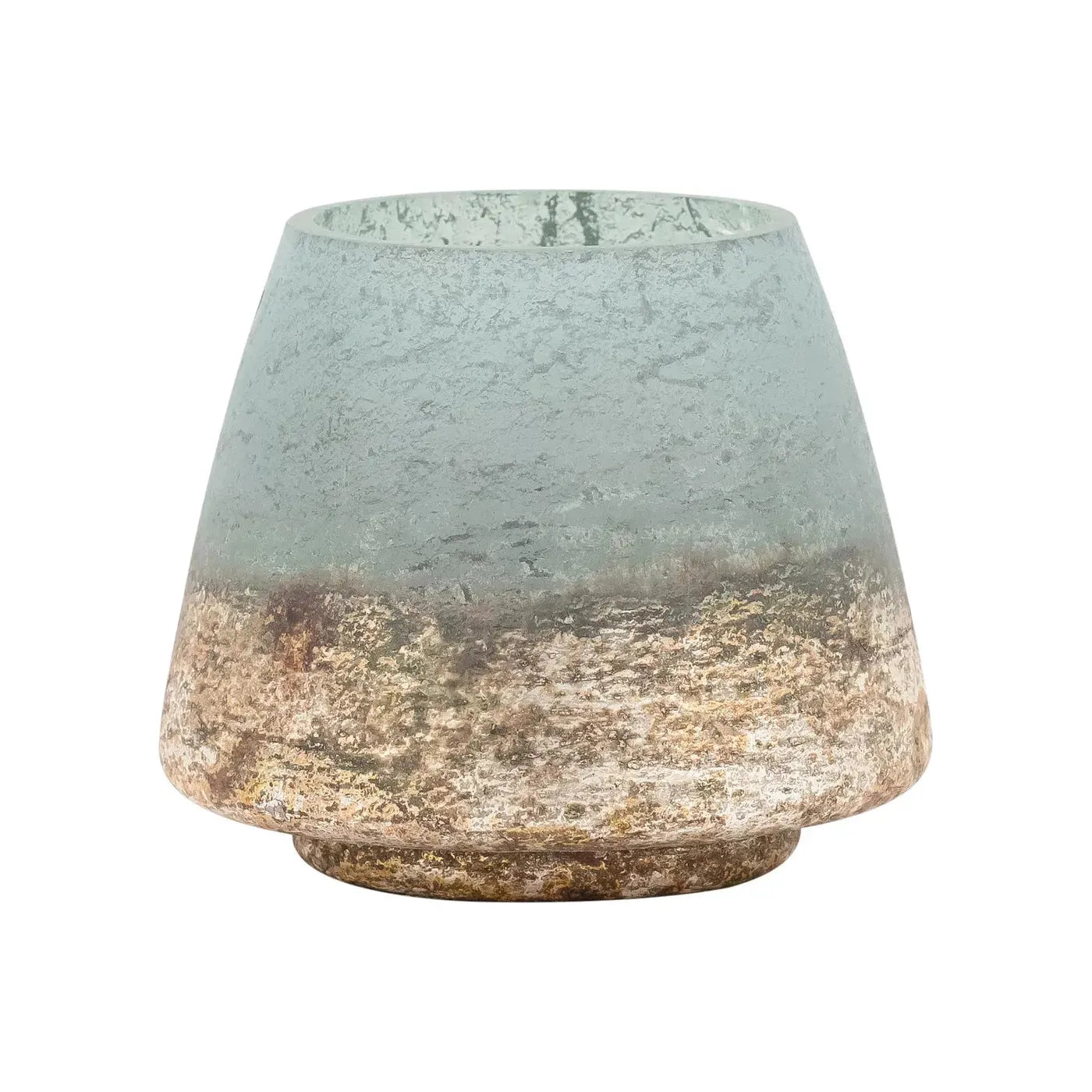 The Cambridge Hurricane Vase is small, round, and tapered with a rough, textured surface. It showcases a gradient color that transitions from seafoam green at the top to earthy brown and beige tones at the bottom. An antiqued gold base adds stability and charm to this versatile home decor piece, which boasts an overall rustic, worn appearance.