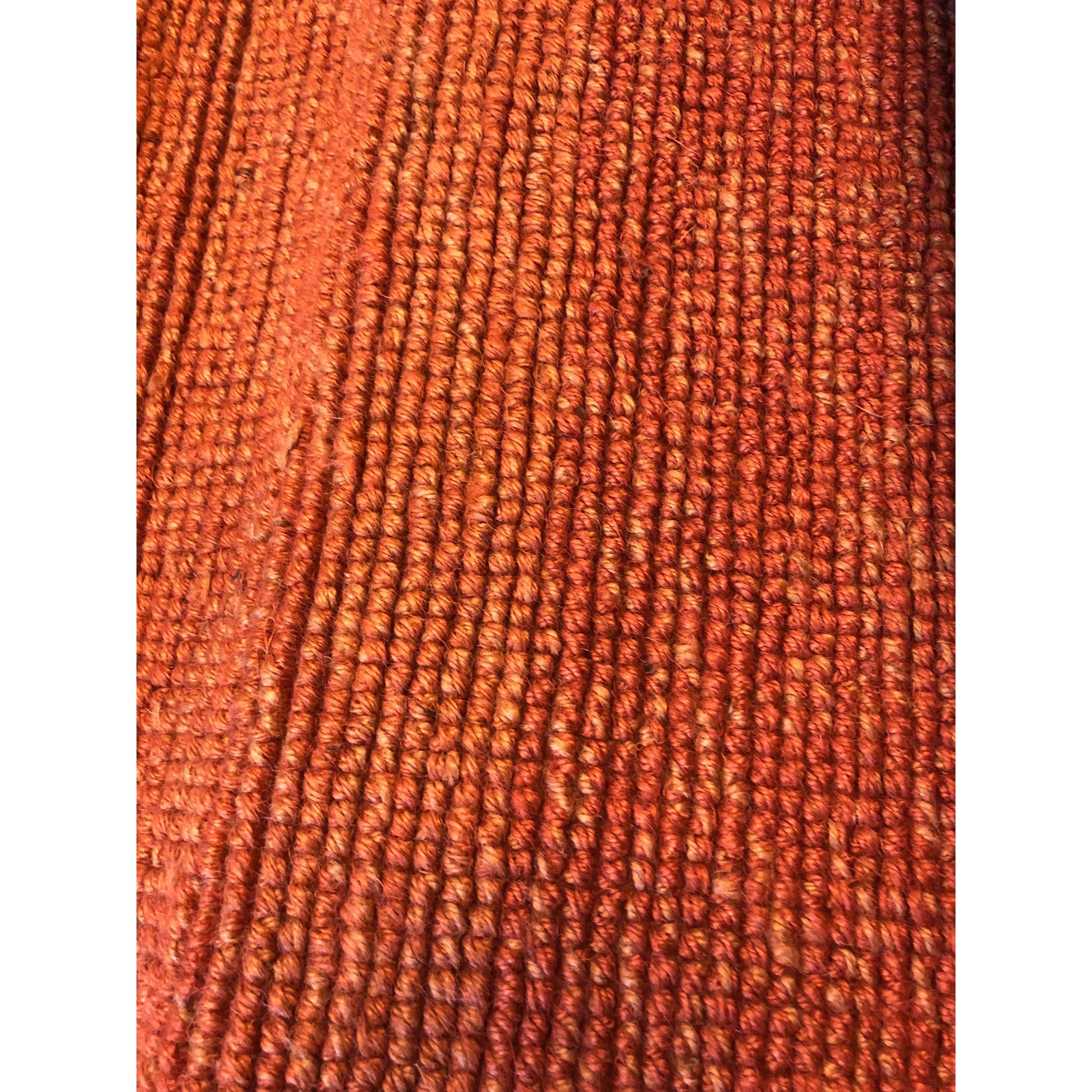 Close-up of the Amco Jute/Cotton Rug reveals a textured, woven surface with parallel orange and red ridges. The tightly knit fibers and subtle gloss create a warm, rich pattern.
