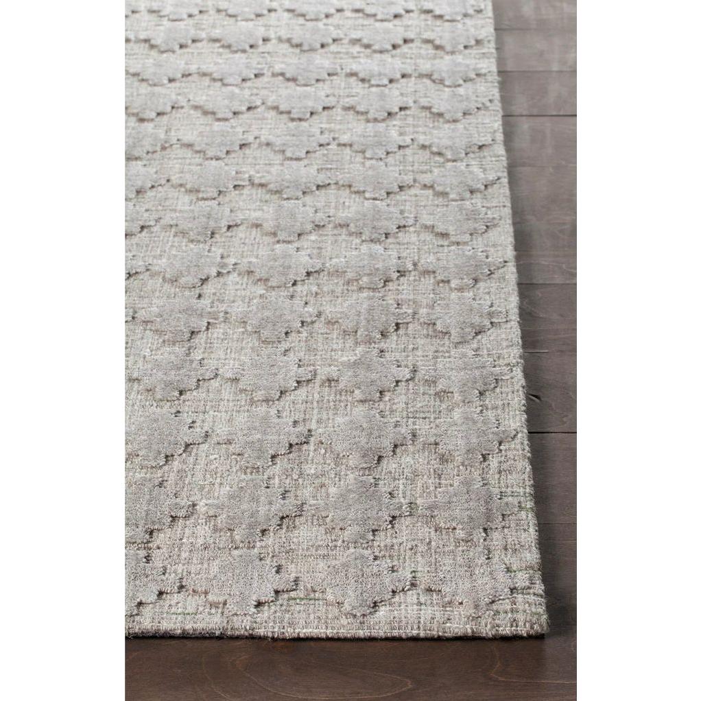 A close-up of the Netix Wool/Viscose Rug, featuring a light gray color and subtle raised geometric pattern of interlocking shapes. The rug is partially visible on a dark wooden floor, showing its edge and textured surface.