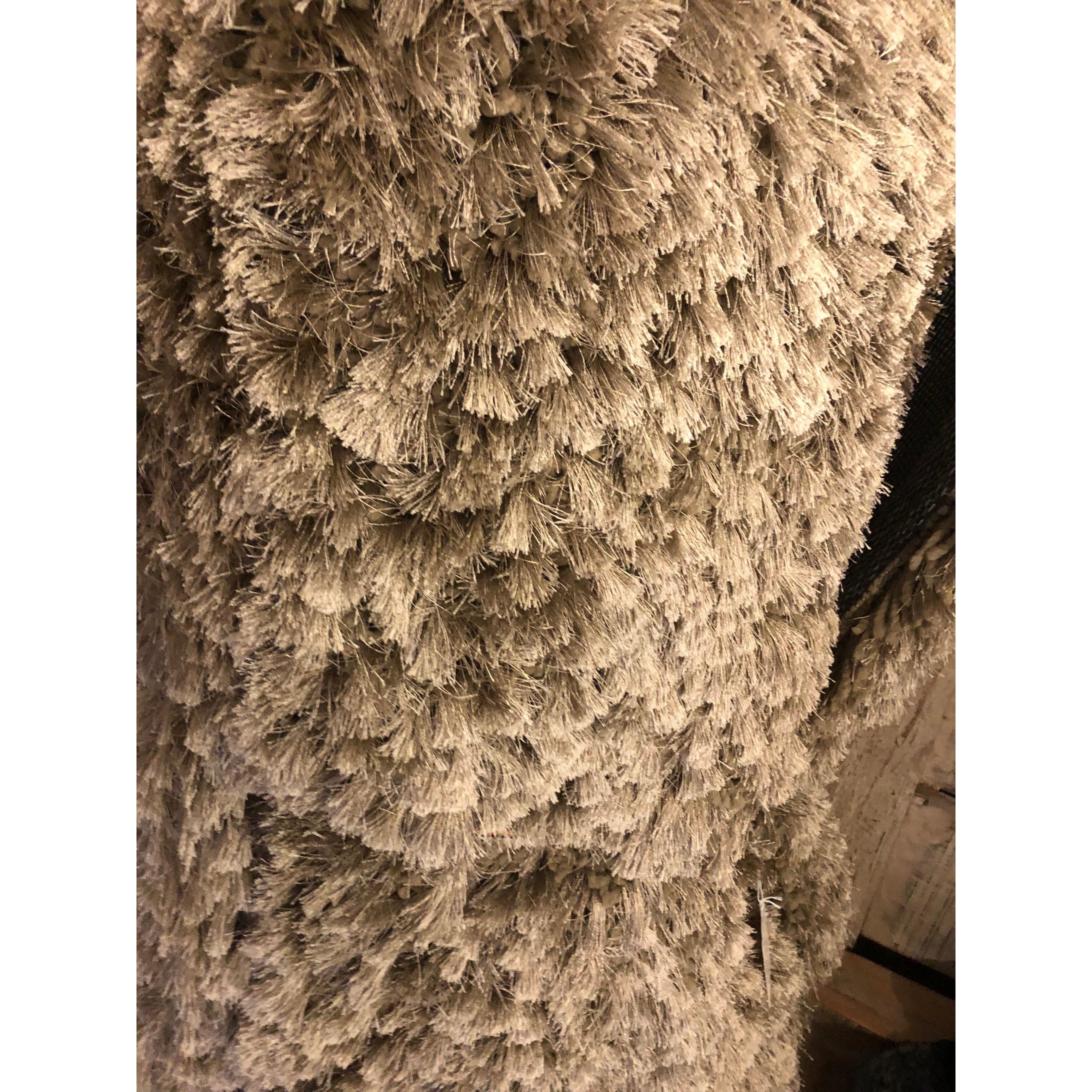 Close-up of the Giulia Polyester Rug's dense, beige, shaggy fibers. The layered texture and clustered bristles are highlighted by the lighting, showcasing the rug's plush and durable surface.