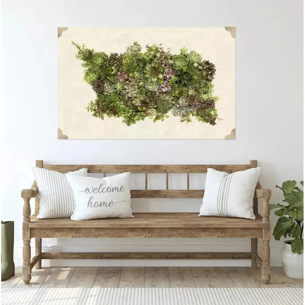 A cozy, rustic wooden bench with three white cushions, including one embroidered with "welcome home," is set against a white wall. Above the bench hangs a rectangular framed vertical garden showcasing an array of succulents and green plants, perfectly positioned using Corner Hangers. Wooden floorboards and a small plant are visible.