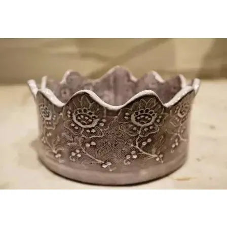 The Casado Crown Vessel is a round, light ceramic bowl with scalloped, crown-like edges and vintage lace patterns embossed around its sides, featuring a slightly rustic, handcrafted appearance.