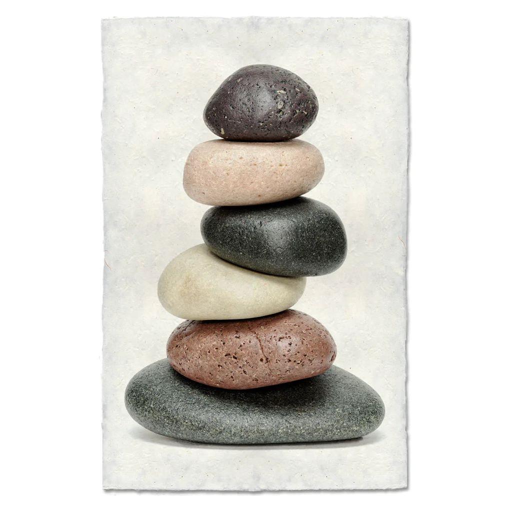 Balanced (2) features a stack of six smooth, oval stones in shades of gray, brown, beige, and black—balanced on handmade Nepalese paper against a textured white background—to evoke calm and balance.