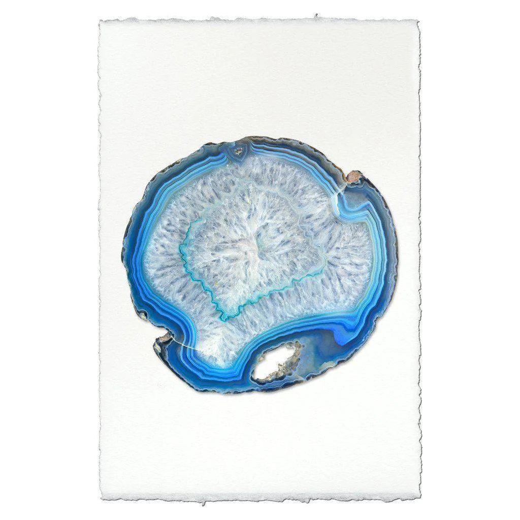 The Azure Agate showcases a cross-section of blue agate with layered blue, white, and gray bands on textured handmade paper. Its circular shape and organic patterns evoke abstract art, complete with a rough and slightly uneven outline.