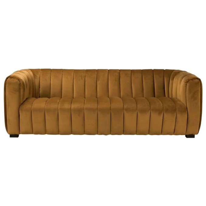 The Donna Upholstered Sofa features plush, mustard brown velvet with a channel-tufted back and arms, highlighting its sculptural curves and modern design. Supported by discreet black legs, it boasts a sleek contemporary look while its smooth upholstery adds luxury.