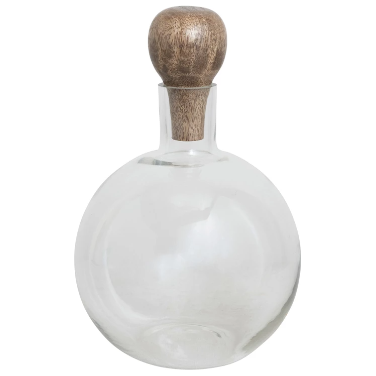 The Decanter with Mango Stopper features a clear, round glass body with a wide base and narrow neck, topped by a smooth light brown mango wood stopper. Ideal for wine lovers, this empty bottle is photographed on a plain white background.