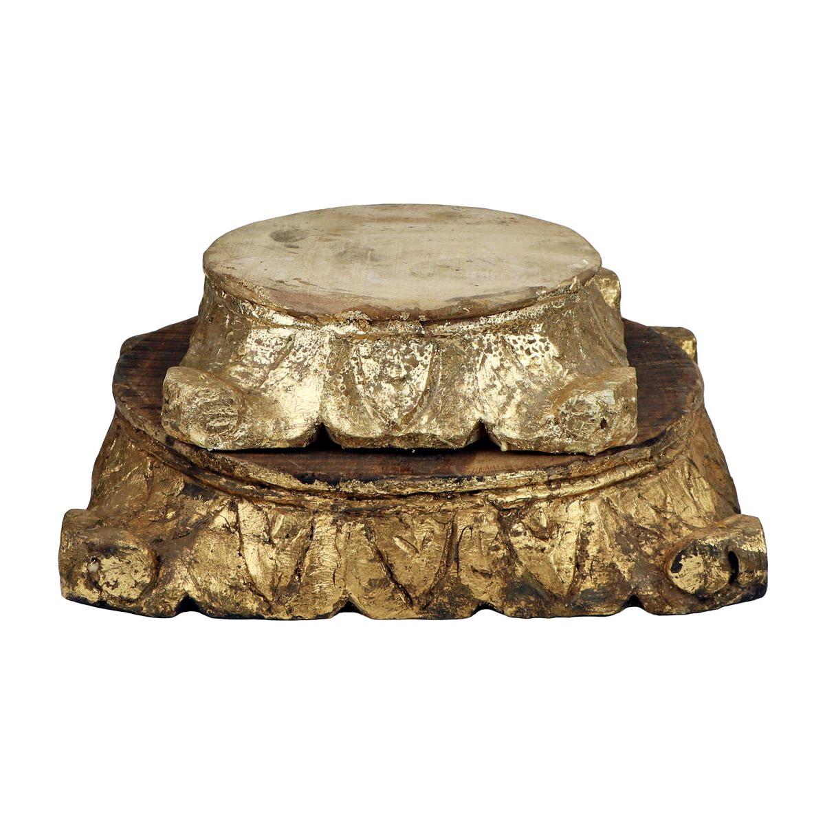 The Carved Pillar Base in natural wood features a round pedestal with hand-carved leaf motifs and a gold finish, supporting a smaller circular top. Its ornate design has an antique, vintage style.
