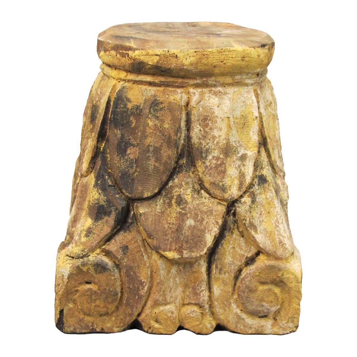 The Carved Pillar Base, Natural Wood, is a square rustic stool with a weathered texture in gold, brown, and black tones. Its ornate pillar base features hand-carved petals and scroll patterns for an antique artistic feel. The flat top is slightly rounded.