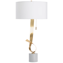 The Gold Ribbon Lamp is a modern table lamp with a tall white cylindrical shade. Its base features an elegant twisted gold metal accent and a cylindrical stand, all in a luxurious gold leaf finish. A delicate gold pull chain hangs below the shade.
