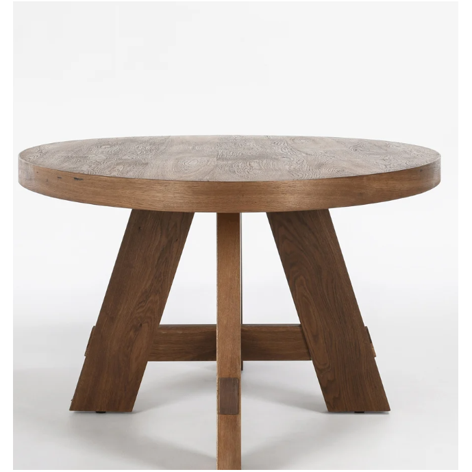 A Kael Oval Dining Table, 46D x 80W x 30H, with a thick, smooth tabletop and a distinctive base. The base features four angled legs that converge at the center and are supported by a crossbeam. The table has a natural wood grain finish, giving it a rustic appearance. It stands against a plain white background.