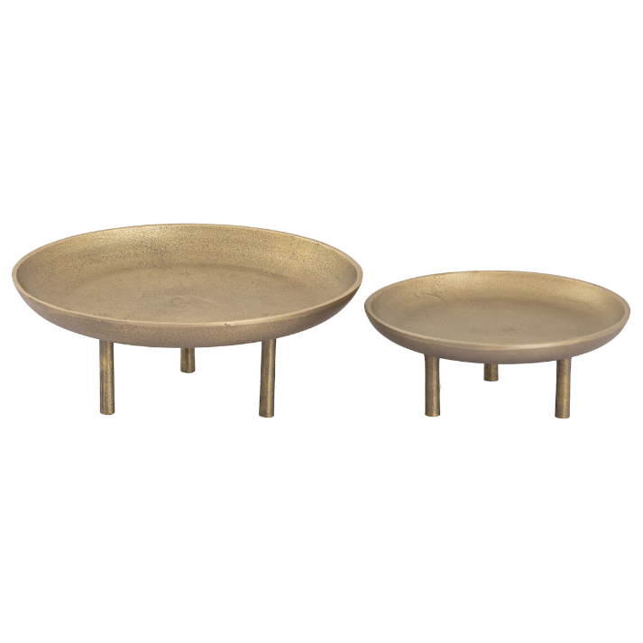 Displayed side by side on three short legs are two round, shallow brass Riser Plates. The Riser Plate on the left is larger than the one on the right, accentuating an oversized scale. Each plate features a matte finish that gives them an antique appearance, creating an ideal elevated display piece set a few inches above the surface.