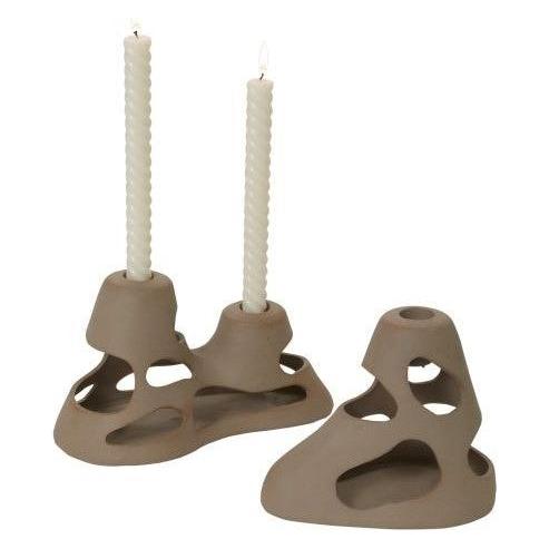 The Bisque Clay Candleholder set includes two sculptural pieces crafted from natural brown bisque clay, resembling ocean-eroded rock. Each features hand-carved hollow sections, one holding a textured white candle. The matte ceramic finish enhances their organic and abstract charm.