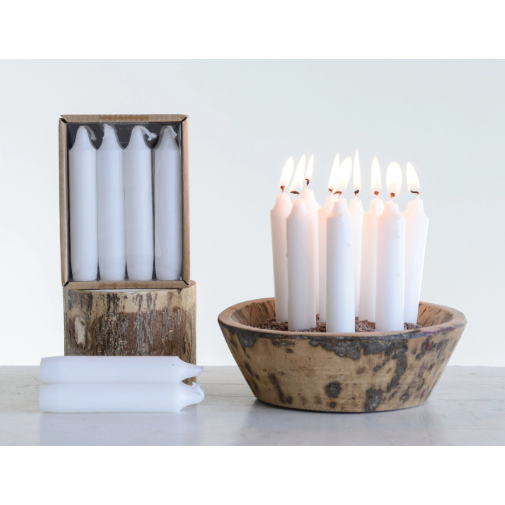 A rustic wooden bowl holds several lit 5" Taper Candles upright. Nearby, an open box shows unlit 5" Taper Candles with three more in front. Each 5" Taper Candle offers a 5-hour burn time on a plain, light background.
