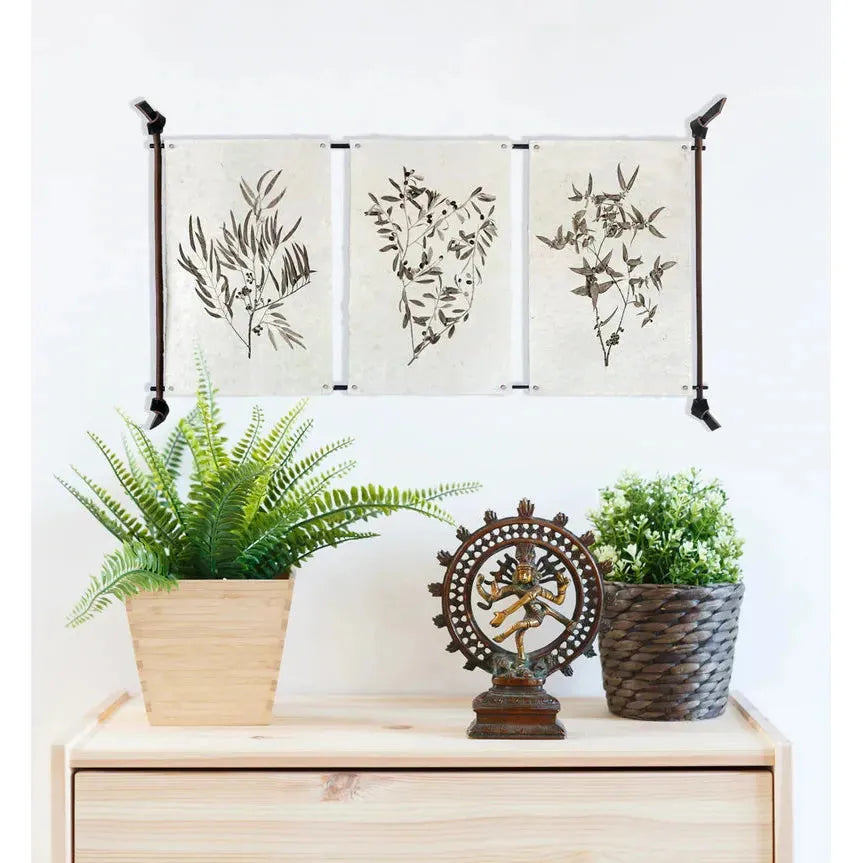 A light wood dresser holds plants and a bronze Shiva statue. Above, white walls are adorned with botanical prints using the 3 Print Hanger, Small Prints Only, for display without damage.